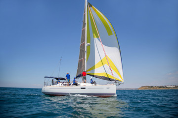 Fototapeta premium A white motor yacht with raised sails takes part in the regatta. A strong wind tipped the ship. Waves, a small wave amplify emotions at competitions. A man, a sailor, a yachtsman is lying on the bow o
