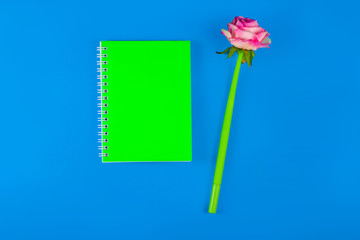 Notepad and pen in the shape of a flower on a blue background. Top view.