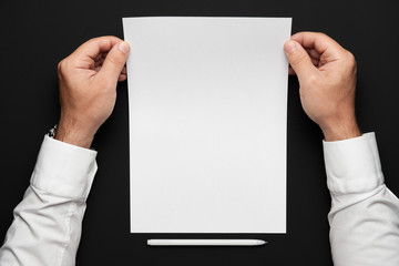 a blank sheet of paper and a businessman's hands on a black table, a white shirt and a wrist watch, a top view-a template for any text or inscription