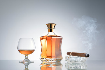 close up view of cigar, bottle of cognac and a glass aside on grey back. 