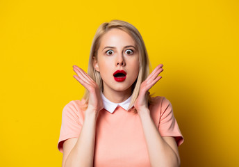 Surprised blonde girl in pink dress on yellow background