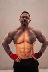 Fototapeta premium Strong and powerful fitness coach posing in a bright studio with hand wraps on, looking serious