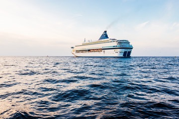Large white cruise liner (passenger ship) sailing in the Riga bay of the Baltic sea at sunset. A...