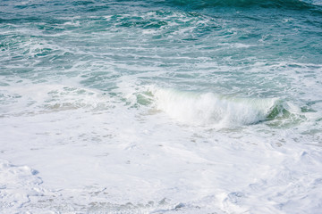 Turquoise ocean water with small white foam waves gently crashing into golden sand beach