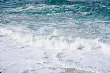 Turquoise ocean water with small white foam waves gently crashing into golden sand beach