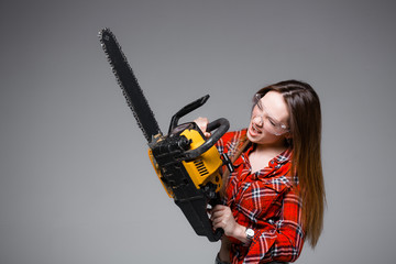 Beautiful sexy girl in red plaid shirt and in transparent glasses holds a chainsaw and crags. Advertising shot for hardware store.