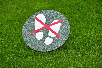 Keep off the grass warning sign over green lawn