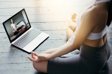 Close-up of a laptop screen with a video tutorial on yoga and a girl in a sports form meditating in...