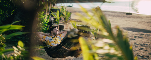 A young man lies in a hammock on a sunny beach.