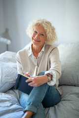 smiling older woman sitting on bed writing in diary