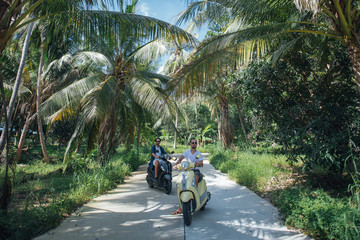 Two men on motorcycles in palm trees on a tropical island