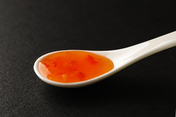 Sweet chilli sause in a white chinese porcelain spoon on a black stone serving board. Sauces and seasonings for meat, fish and vegetables.