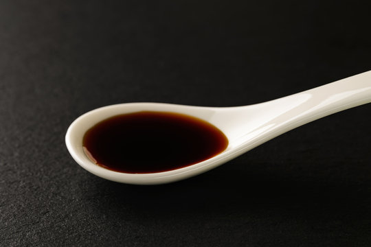 Classic soy sauce in a white chinese porcelain spoon on a black stone serving board. Sauces and seasonings for meat, fish and vegetables.