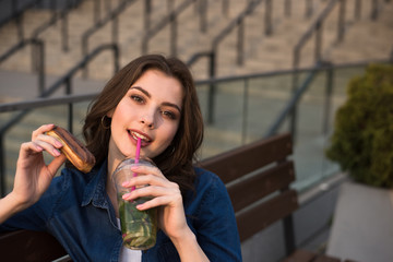 young beautiful woman is enjoying with cake and drink sitting on city bench