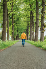 Man in yellow jacket and jeans walks on country road in springtime.