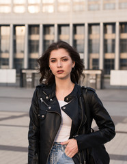 Plakat portrait of pretty brunette woman in leather jacket on city background