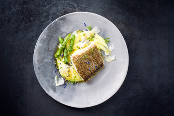 Traditionell gebratenes Skrei Kabeljau Fisch Filet mit grünen Spargel Spitzen und Kartoffel Püree Creme in Parmesan Olivenöl Sauce als Draufsicht auf einem  Modern Design Teller mit Textfreiraum