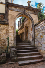 Naklejka premium Old Italian courtyard. Wall with arch and stairs and weaving plants