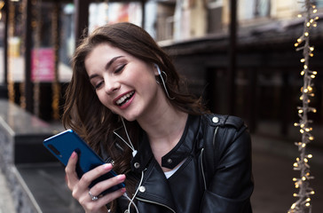 young pretty woman talks on mobile phone in an earphones and laughs on cafe background