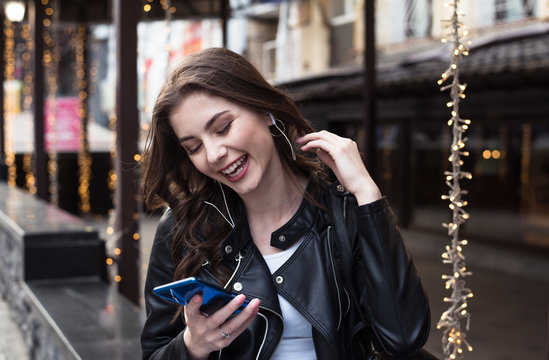 young pretty woman talks on mobile phone in an earphones and laughs on cafe background