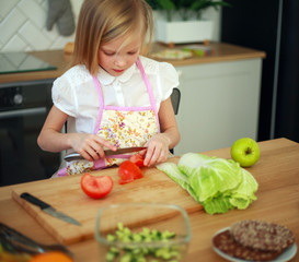 Little girl child cuts tomatoes cooks salad at table in kitchen, healthy food