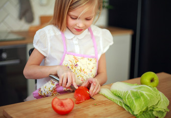 Little girl child cuts tomatoes cooks salad at table in kitchen, healthy food