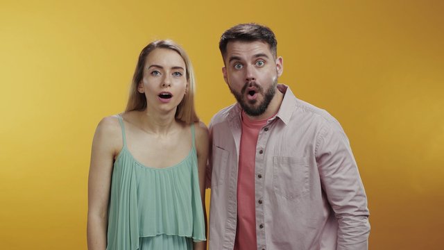 Handsome young man and woman searching for something point at camera look surprised eyes wide open admiring posing isolated on background. Couple together. Family portrait.