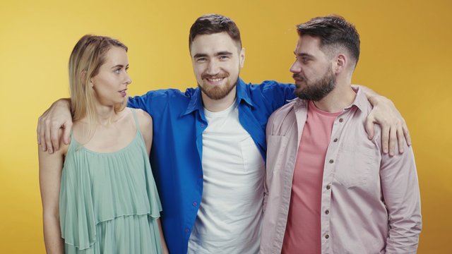 Caucasian Young Couple Of Lovers Holding Hands Posing On Background. Third Wheel Jealous Bearded Friend Embracing Separating Man And Woman. Love Triangle.