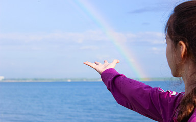 Portrait of a girl who stretches out her hand to the rainbow over the lake.