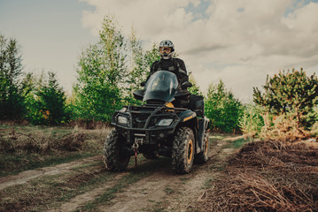 Fototapeta premium A young man in a white helmet rides through the woods on a Quad bike. Extreme hobby. A trip to ATV on the road from logs. Quad Biking through the forest.