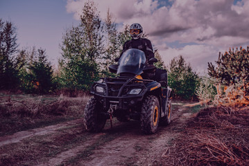 Fototapeta premium A young man in a white helmet rides through the woods on a Quad bike. Extreme hobby. A trip to ATV on the road from logs. Quad Biking through the forest.