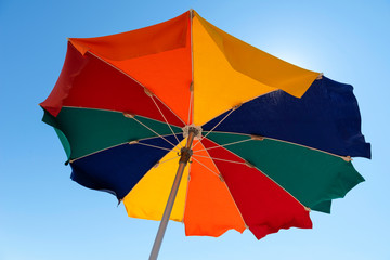 Bright colorful beach umbrella against the blue sky. Beach vacation.
