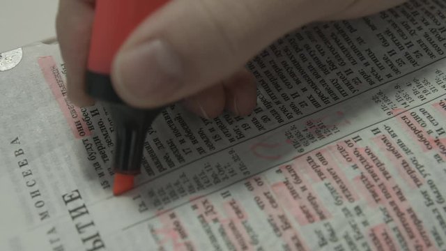 A young man reads the Bible and with an orange marker highlights interesting Bible verses.