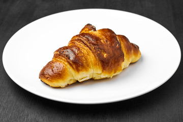  Fresh croissant with a brown crust on a white plate on a black table.
