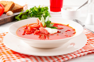 red Ukrainian vegetable soup, borscht with sour cream and parsley in a white plate on a checked towel,