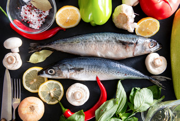 2 raw mackerel fish with chili pepper, lemon slices, tomato,  zucchini, onion, Basil, mushrooms and spices, fork, knife on a black background,  top view,