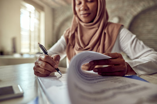 Close-up of Muslim businesswoman signing documents in the office.