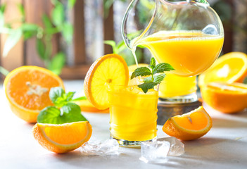 Fresh orange juice, orange slices, mint leaves and ice on a wooden table.