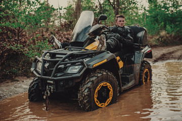Fototapeta premium A young man in a white helmet rides through the woods on a Quad bike. Extreme hobby. A trip to ATV on the road from logs. Quad Biking through the forest.