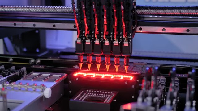 Automatic SMD pick and place machine during work - assembly of computer printed circuit board at factory. Automated technology, industrial, robotic, electronic, production, manufacturing concept
