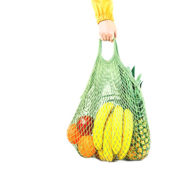 Delivery of grocery. Hand holds mesh shoper bag with fresh fruit and vegetables green produce. Eco friendly lifestyle and shopping. Healthy eating vegetarian, zero waste concept. Copy space. isolated