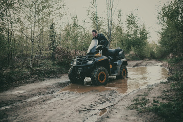 Fototapeta premium A young man in a white helmet rides through the woods on a Quad bike. Extreme hobby. A trip to ATV on the road from logs. Quad Biking through the forest.