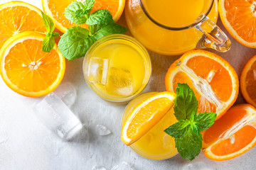 Fresh orange juice, orange slices, mint leaves and ice on a wooden table.