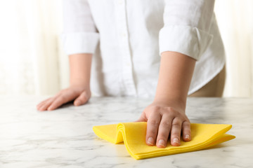 Woman wiping white marble table with rag indoors, closeup