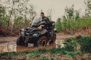 Fototapeta premium A young man in a white helmet rides through the woods on a Quad bike. Extreme hobby. A trip to ATV on the road from logs. Quad Biking through the forest.