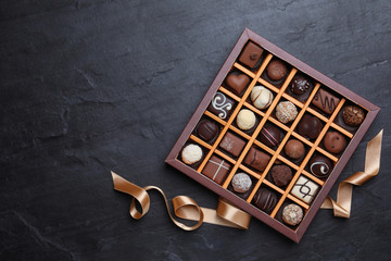 Box with delicious chocolate candies on black table, flat lay. Space for text