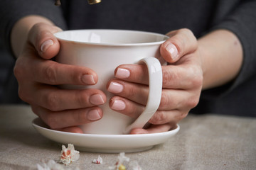 Close-up of female hands with a mug of beverage. Beautiful girl in grey clothes holding cup of tea or coffee.