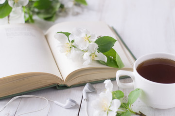 Apple blossom on book, cup of tea, head phones on wooden table 