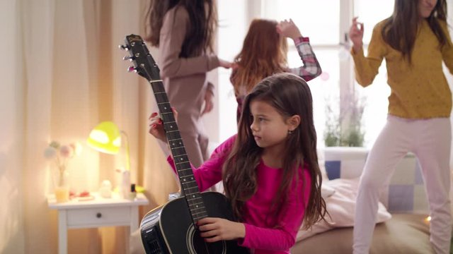 Group of small girls friends playing guitar and jumping on slumber party.