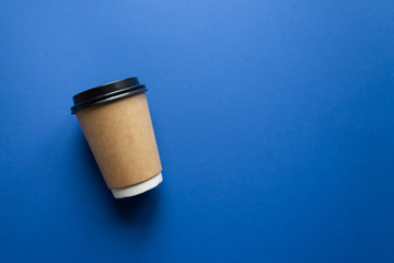 Coffee to go concept. Disposable craft cup with black plastic cover on a trendy classic blue background. Place for text. Flat lay style. Top view